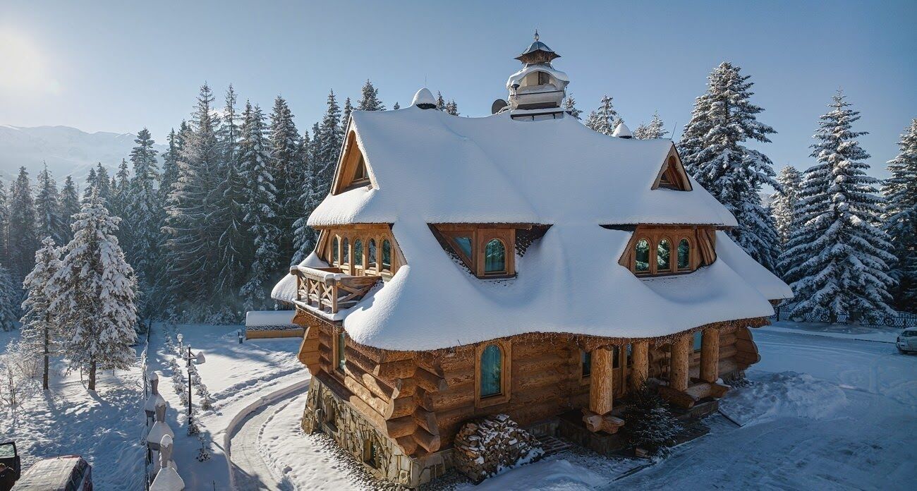 A log cabin with a snow-covered roof, wooden balconies, and a traditional design.