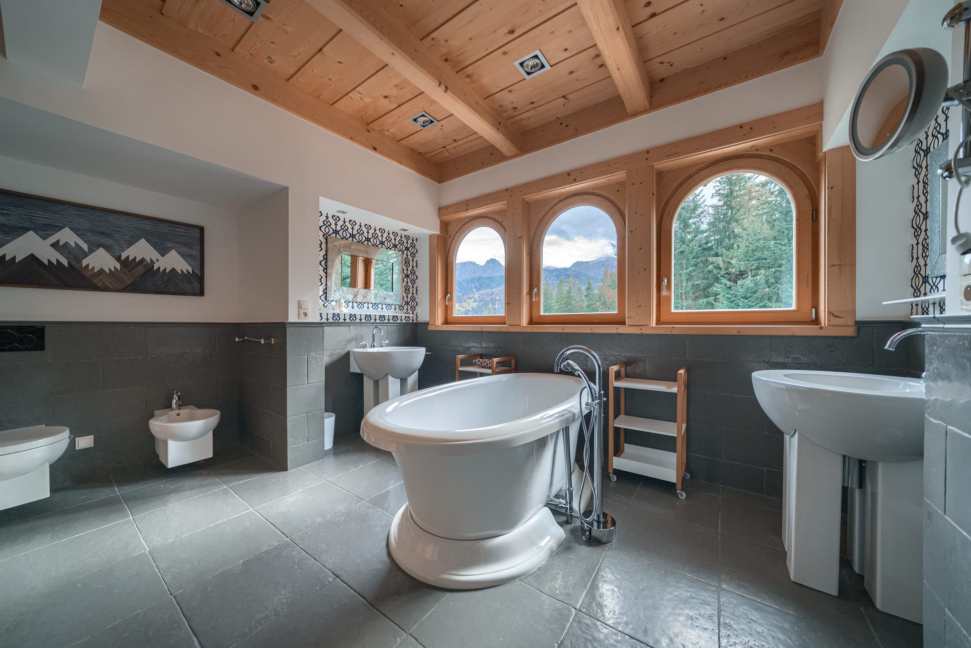 A modern bathroom with a freestanding bathtub, two sinks, and a large window with a mountain view.