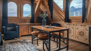 Una habitación acogedora con una mesa de madera, dos sillas, un sofá azul y un ventanal con vistas a la montaña.