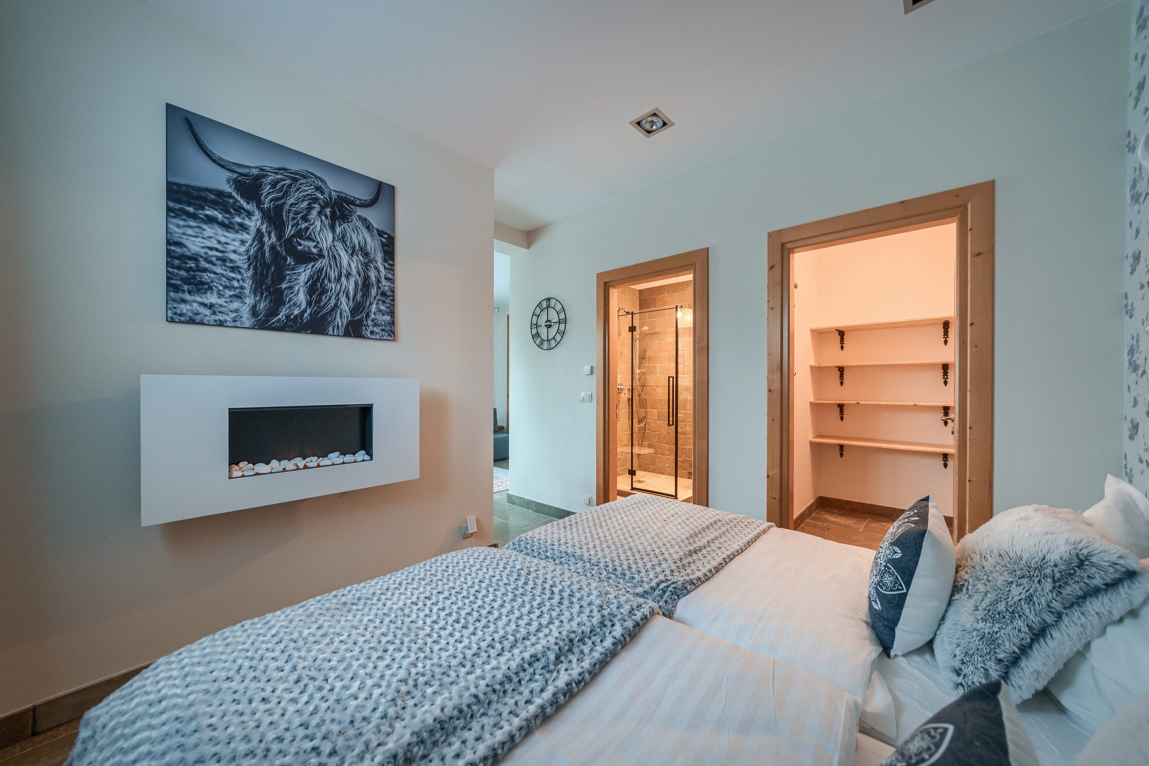 Um quarto com uma cama, uma prateleira fixada na parede com objetos decorativos e uma porta de entrada para um banheiro.