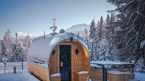 Una cabaña de madera cubierta de nieve con techo curvo, una puerta y un pequeño porche.