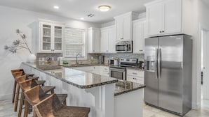 A modern kitchen with white cabinets, stainless steel appliances, a granite countertop, and wooden bar stools.