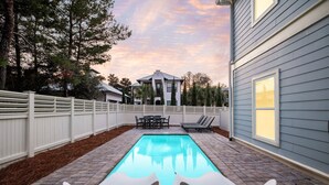 A backyard with a swimming pool, a white fence, and a house in the background.