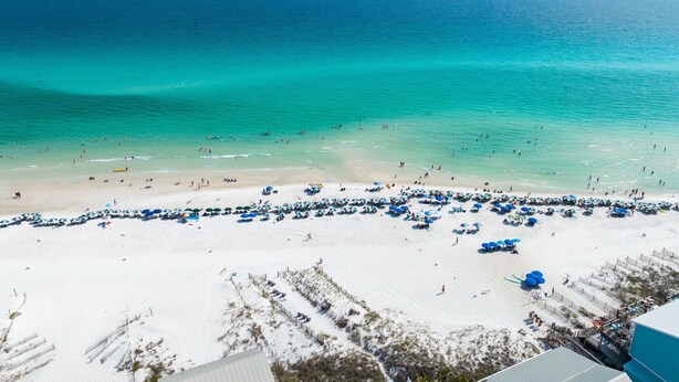 A beach with clear turquoise waters, a sandy shore, and numerous blue umbrellas.