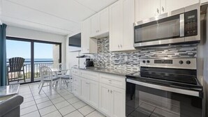 A modern kitchen with white cabinets, a stainless steel microwave, and an oven. There is a dining area with a table and chairs, and a view of the ocean through large windows. - Beacher's Oceanfront Balcony Suite with Onsite Front desk and staff (St. Augustine)