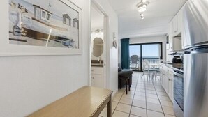 A modern kitchen with white cabinets, a stainless steel refrigerator, and a dining area with a table and chairs. - Beacher's Oceanfront Balcony Suite with Onsite Front desk and staff (St. Augustine)