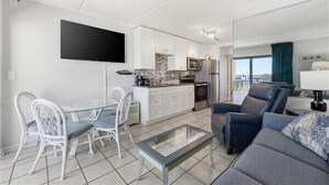 A modern living room with a glass coffee table, a sofa, and a dining area with white chairs. - Beacher's Oceanfront Balcony Suite with Onsite Front desk and staff (St. Augustine)