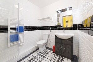 A bathroom with white subway tiles, a black and white patterned floor, a white toilet, a sink, and a shower.