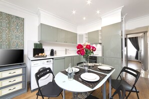 Una cucina moderna con zona pranzo, mobili bianchi, una TV a schermo piatto e un vaso con fiori.