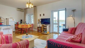 A living room with a sofa, a coffee table, a TV, and a dining area with chairs and a table. - Apartment with sea view, large terrace, garden, parking, air conditioning in every room (Mali Lošinj)
