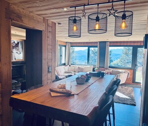 A wooden dining area with a large table, chairs, and hanging light fixtures.