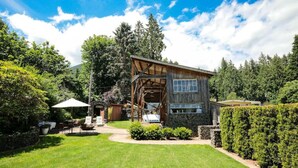 A rustic wooden cabin with a stone foundation, surrounded by a well-maintained lawn and dense forest. - Your next outdoor oasis (Brinnon)