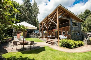 A rustic wooden cabin with a covered patio, outdoor seating, and a stone wall. - Your next outdoor oasis (Brinnon)