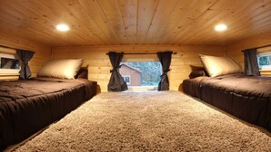 Camera da letto in una baita con due letti, pavimento in moquette, pareti in legno e una finestra con tende.