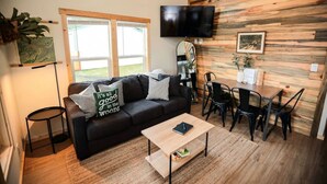 A modern living room with a black leather sofa, a wooden coffee table, and a dining area with black chairs. - Tiny home in the heart of Forks w/starlink & yard (Forks)