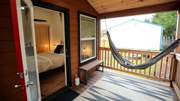 A wooden cabin with a bedroom featuring a bed, a bench, and a hammock on the porch. - Tiny home in the heart of Forks w/starlink & yard (Forks)