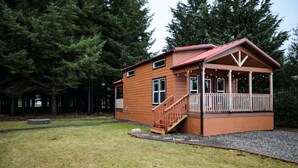 A wooden cabin with a porch and a staircase, surrounded by trees. - Tiny home in the heart of Forks w/starlink & yard (Forks)