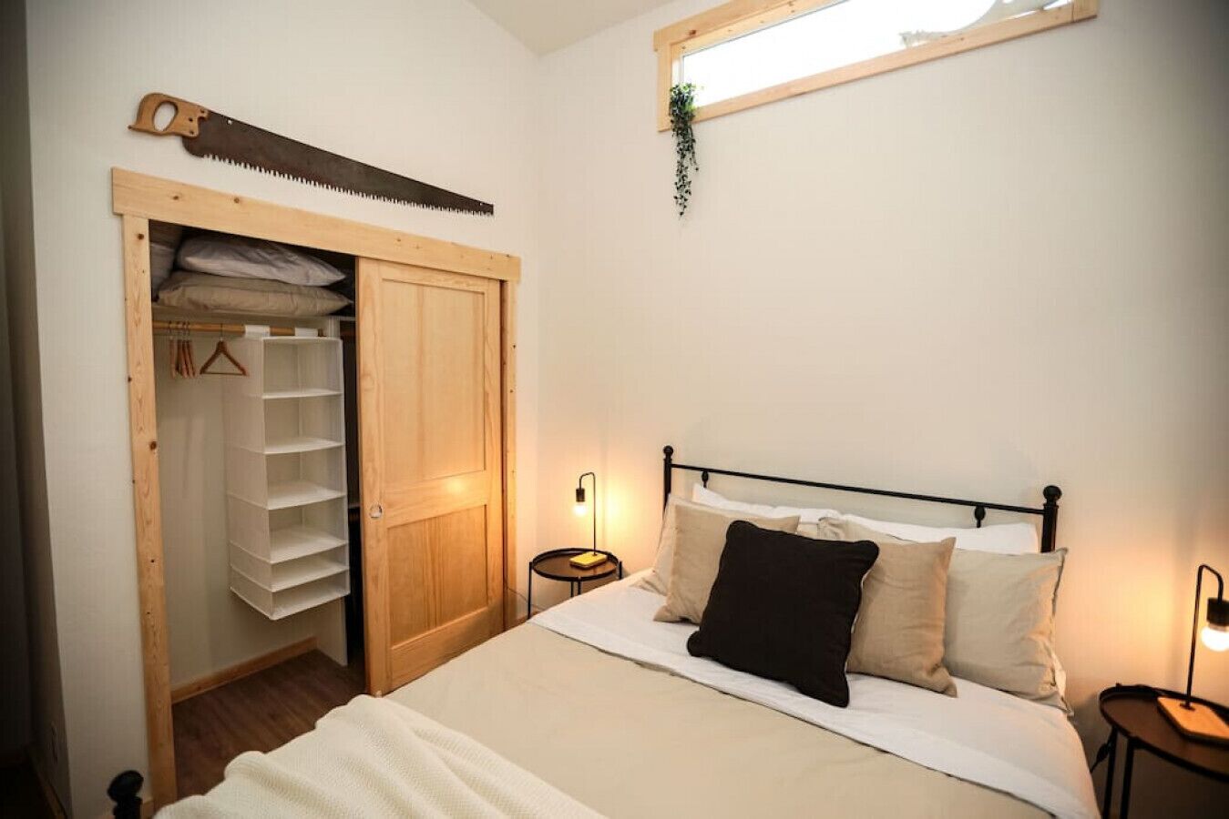 Un dormitorio con cama, mesitas de noche, un armario de madera y una planta colgante.