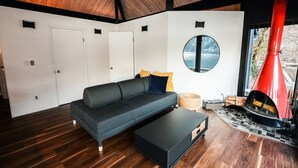 Una sala de estar moderna con un sofá oscuro, un ventanal redondo y una chimenea roja.