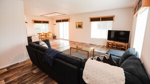 A modern living room with a sectional sofa, a coffee table, a TV, and a dining area with chairs and a table. - Your perfect Base Camp: Central, pet friendly w/ Starlink (Forks)