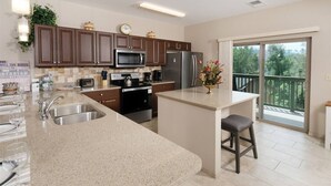 Una cocina moderna con encimeras de granito, electrodomésticos de acero inoxidable y una isla grande con un taburete de bar.