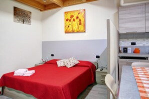 Una camera da letto con una coperta rossa, un quadro appeso al muro e un angolo cottura.