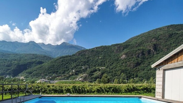 A swimming pool with a mountain view, a wooden building, and a stone wall. - Studio 'Agriturismo L'isola Del Cavallo 2' with Mountain View, Shared Garden and Wi-Fi (Talamona)