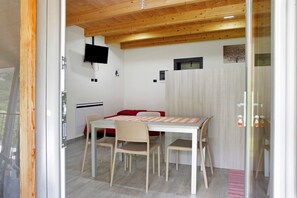 Una stanza con soffitto in legno, un tavolo bianco con quattro sedie, un divano rosso e una TV montata a parete.