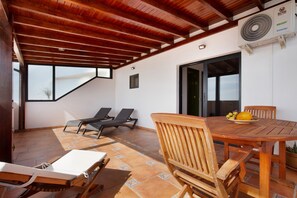 A covered patio with a wooden table and chairs, two lounge chairs, and a fan. - Vacation Home "Las Vistas" with Sea View, Private Terrace & Wi-Fi (Gran Tarajal)