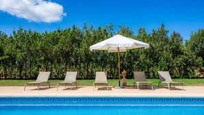 Una piscina con sillas de descanso y una sombrilla blanca.