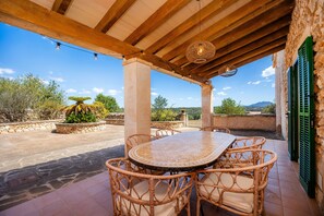 Une terrasse extérieure avec une table ronde et des chaises en osier, un mur de pierre et une vue sur le paysage.
