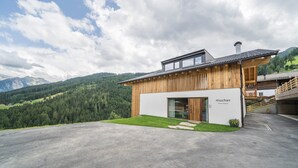 A modern building with a wooden facade, a glass entrance, and a view of a mountainous landscape. - Apartment 'Mucher Veit' with Mountain View, Shared Garden and Wi-Fi (Moso in Passiria)