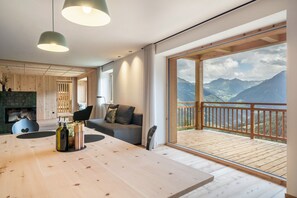 A modern interior with a wooden dining table, a sofa, and a balcony with a mountain view. - Apartment 'Mucher Veit' with Mountain View, Shared Garden and Wi-Fi (Moso in Passiria)