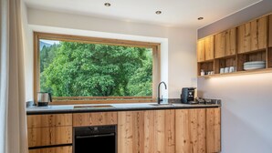 A modern kitchen with wooden cabinetry, a built-in oven, a sink, and a window overlooking a forest. - Apartment 'Mucher Veit' with Mountain View, Shared Garden and Wi-Fi (Moso in Passiria)