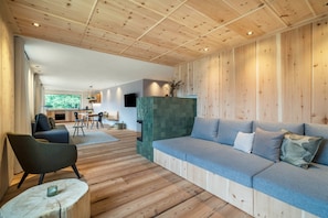 A modern interior with a wooden floor, a grey sofa, a dining area, and a kitchen in the background.