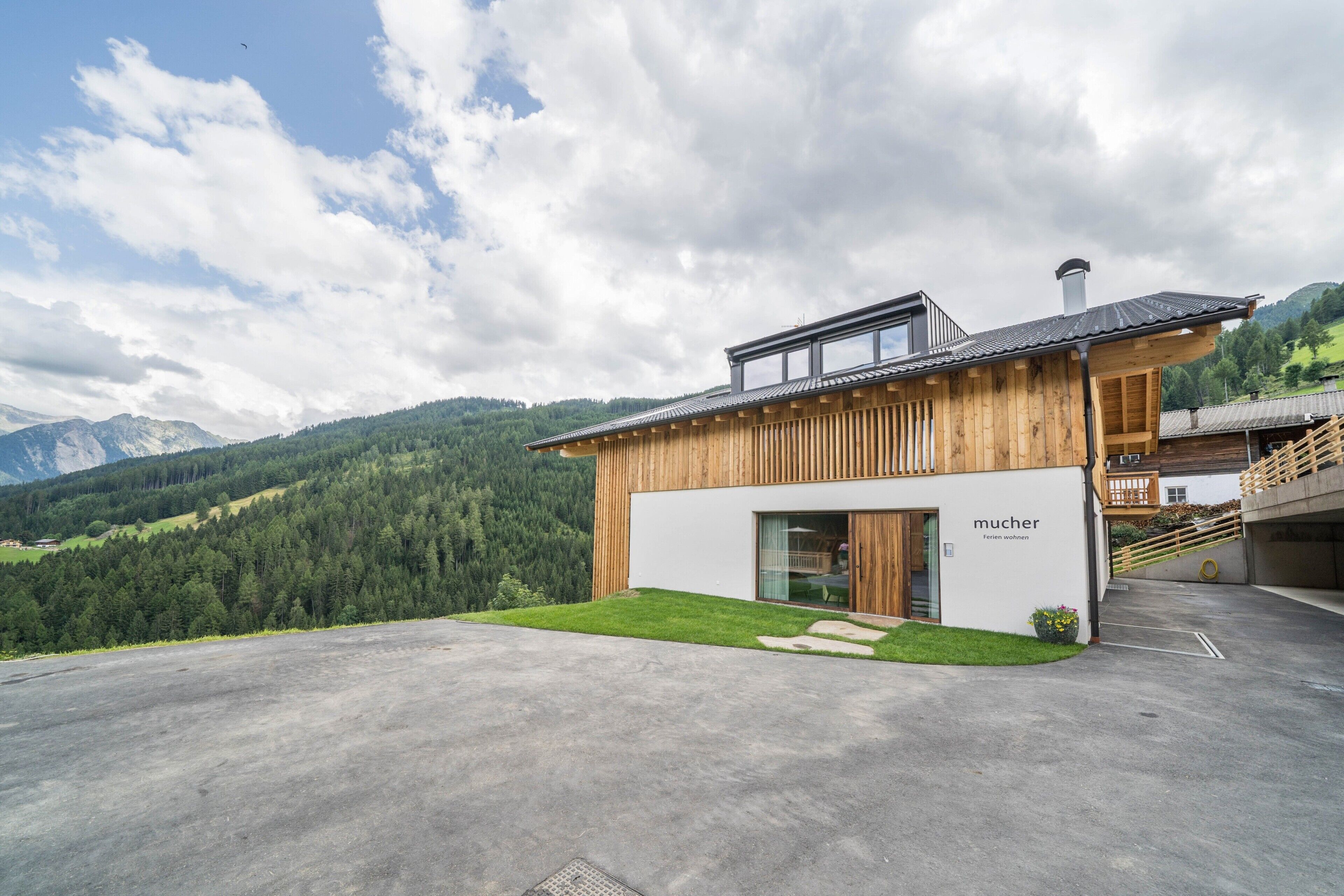 A modern building with a wooden facade, a glass entrance, and a view of a mountainous landscape.