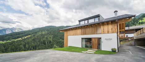 A modern building with a wooden facade, a glass entrance, and a view of a mountainous landscape.