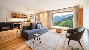 Een moderne woonkamer met een bank, een stoel, een kleine tafel en uitzicht op bergen door grote ramen.