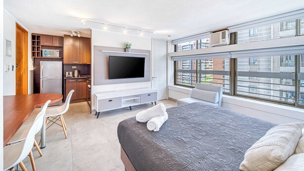 Una habitación de hotel moderna con cama, televisor, comedor y cocina.
