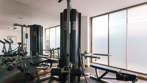 Un gimnasio con equipos de ejercicio variados, ventanas amplias y un banco.