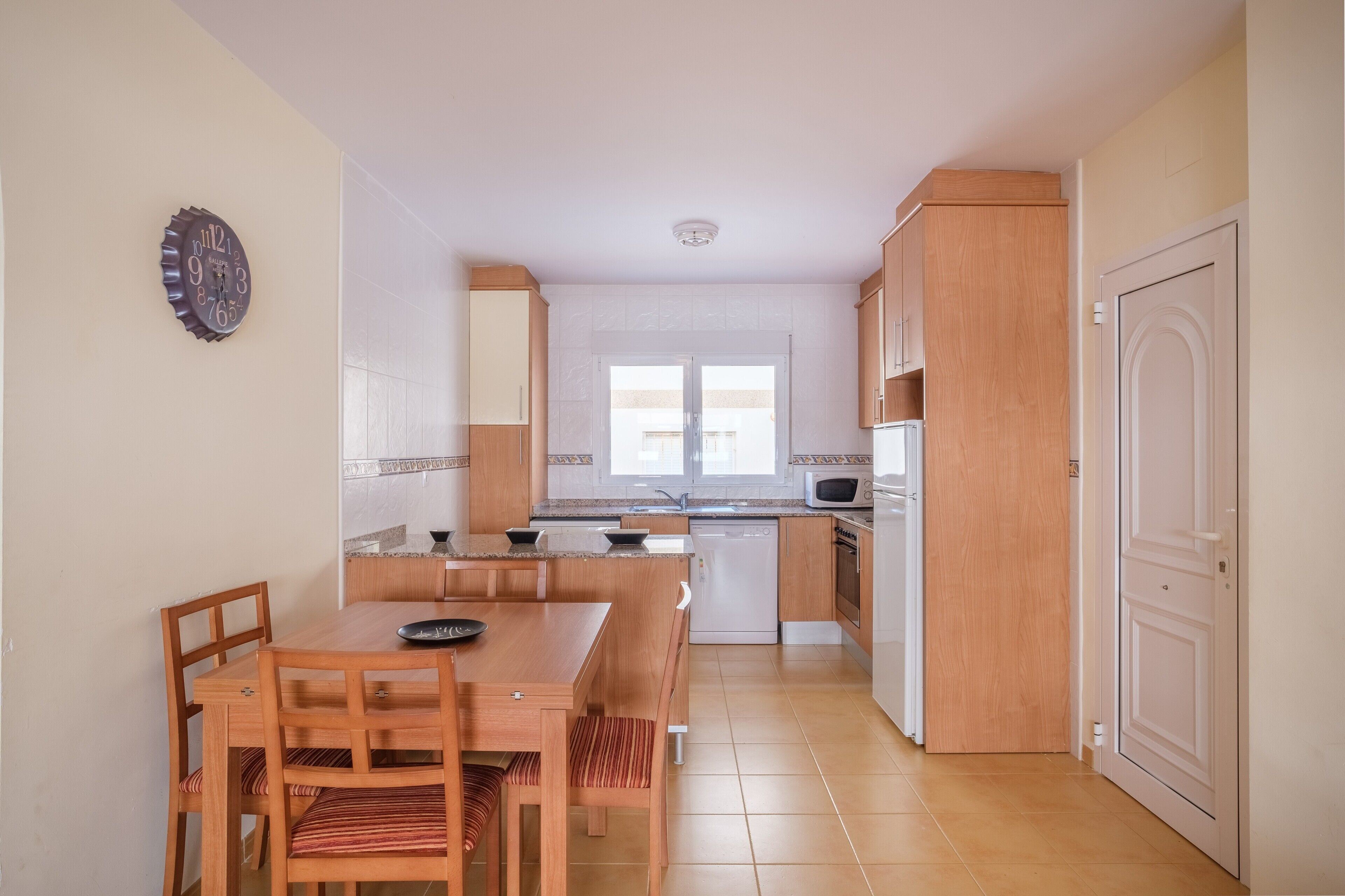 Une cuisine compacte avec des meubles en bois, une table à manger avec des chaises, un four à micro-ondes et un lave-vaisselle.