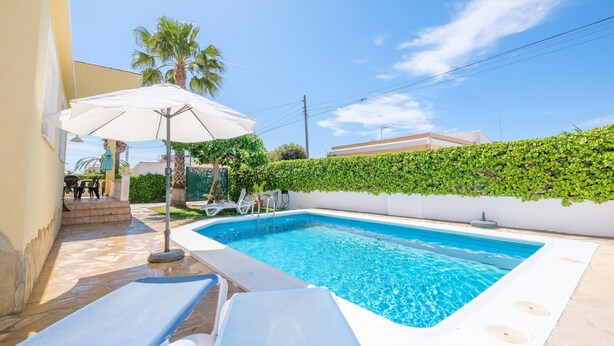 Une piscine avec des chaises longues, un parasol et une haie.