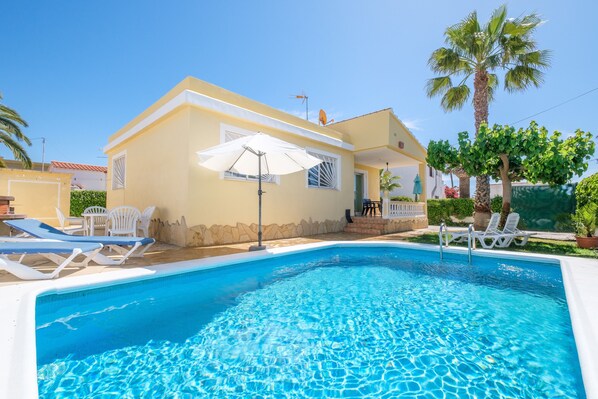 A poolside area with lounge chairs, a pool, and a building with a balcony.