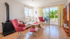 Un salon avec un poêle en bois noir, un canapé blanc, des fauteuils rouges, une table basse en bois et une porte-fenêtre coulissante donnant sur un balcon.