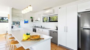 Een moderne keuken met witte kasten, een centraal eiland met krukken, een roestvrijstalen koelkast en een groot raam met uitzicht op groen.