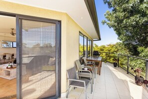 Enjoy dining al fresco on this spacious balcony with a glass door leading to a dining area, surrounded by lush trees and greenery.