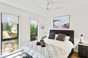 A bedroom with a bed, a ceiling fan, a nightstand, a lamp, and a painting on the wall.