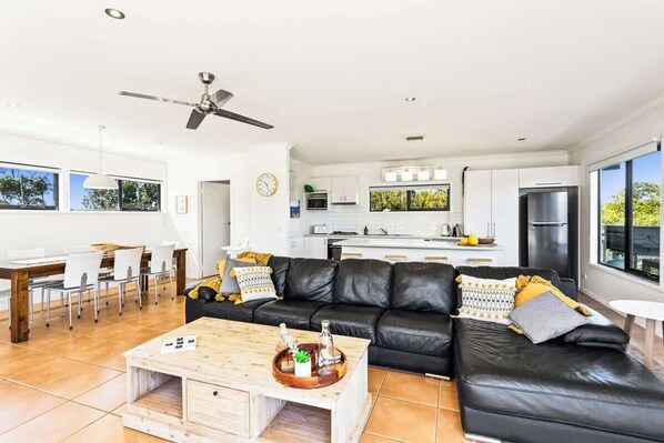 A modern living room with a black leather sofa, wooden coffee table, and a dining area with white chairs.