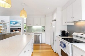 A modern kitchen with white cabinetry, a central island, a dishwasher, a stove, and a refrigerator. - 5BR Modern Beach House Oasis (Cowes)