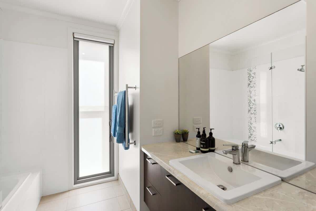 A modern bathroom with a large mirror, two sinks, and a shower.